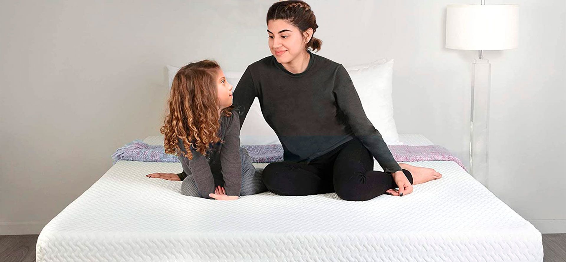 Two sisters sit on a wide mattress.