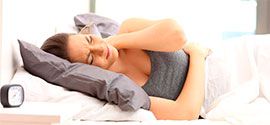 A woman with body pain lies on a mattress for fibromyalgia.