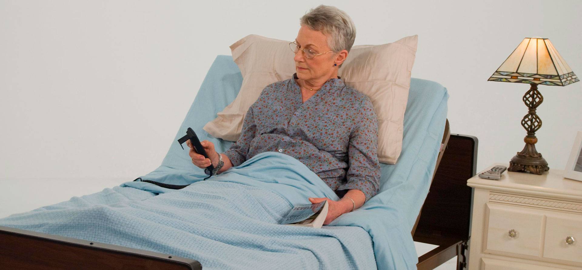 An elderly woman is reading lying on a mattress.