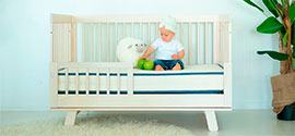 The baby is sitting in a crib on an organic mattress.