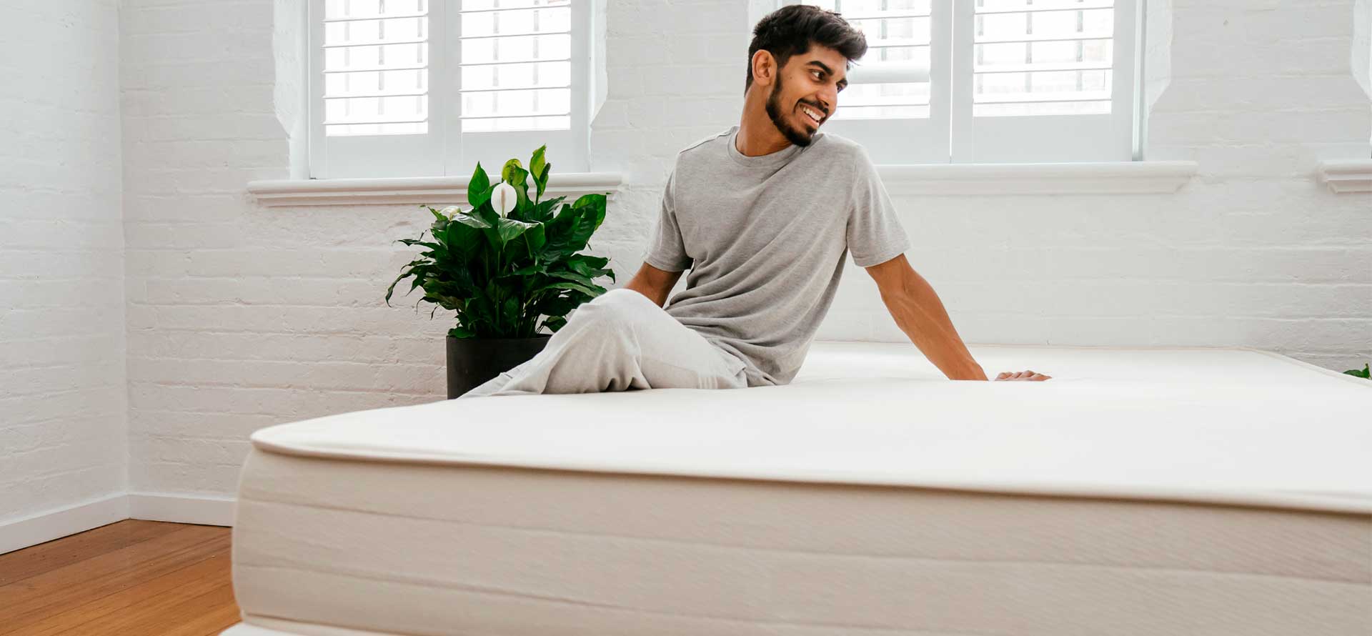 A man sits on an organic mattress in room.
